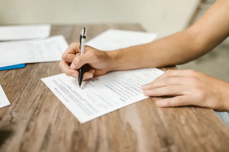Main qui remplit au stylo un formulaire administratif sur un bureau en bois