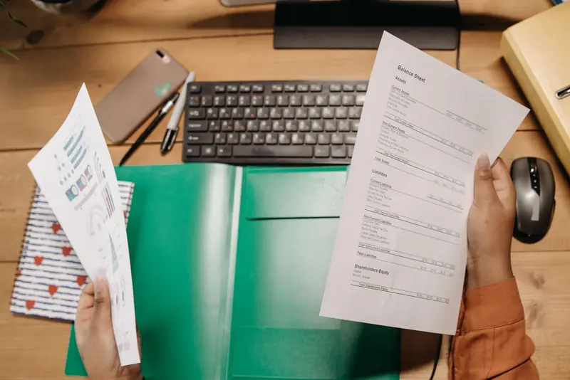Mains tenant un bilan comptable et une page de graphiques au-dessus d'un bureau