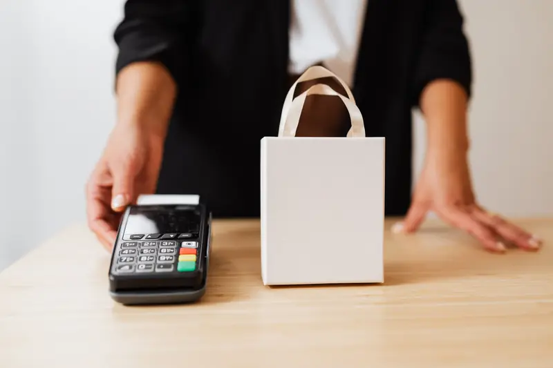 Vendeuse derrière un comptoir tendant un terminal de paiement, à côté d'un sac cadeau
