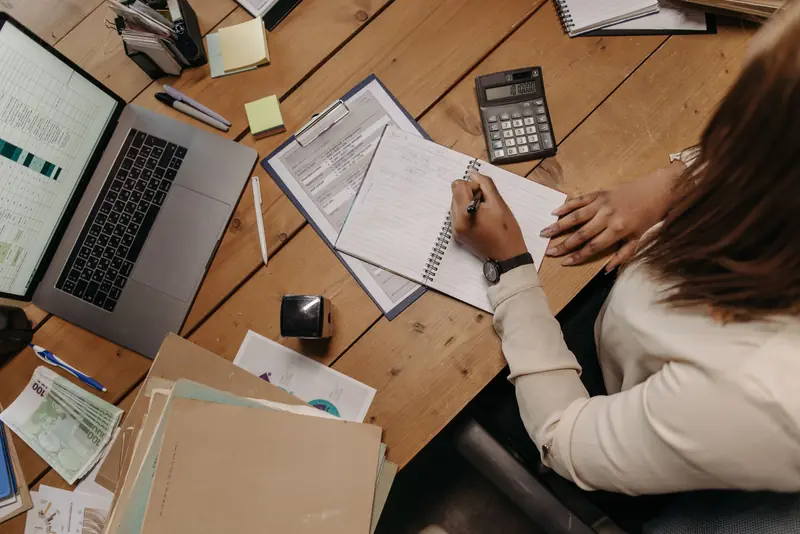 Bureau de cabinet comptable vu de dessus : ordinateur portable, porte-bloc avec une fiche de ratios, calculatrice et chemises cartonnées