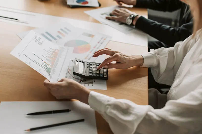 Mains sur une calculatrice, tenant des graphiques imprimés, sur une table de réunion