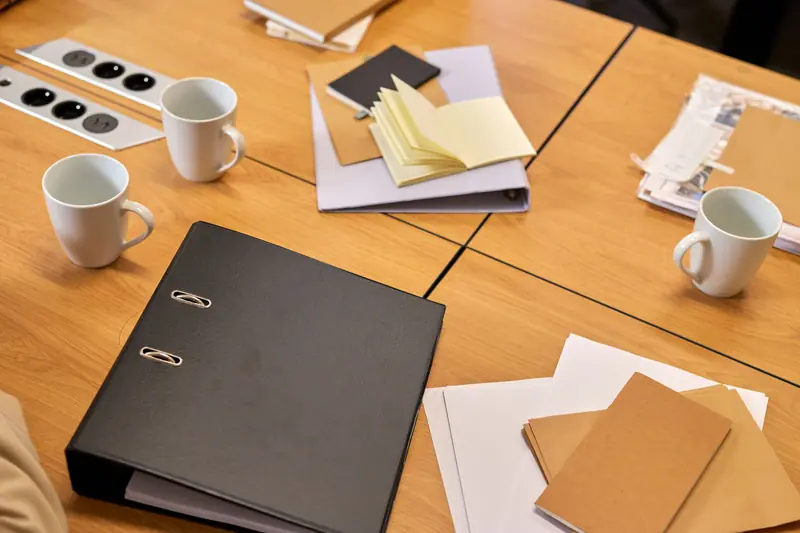 Table de réunion avec un classeur, des carnets, des dossiers et des tasses de café